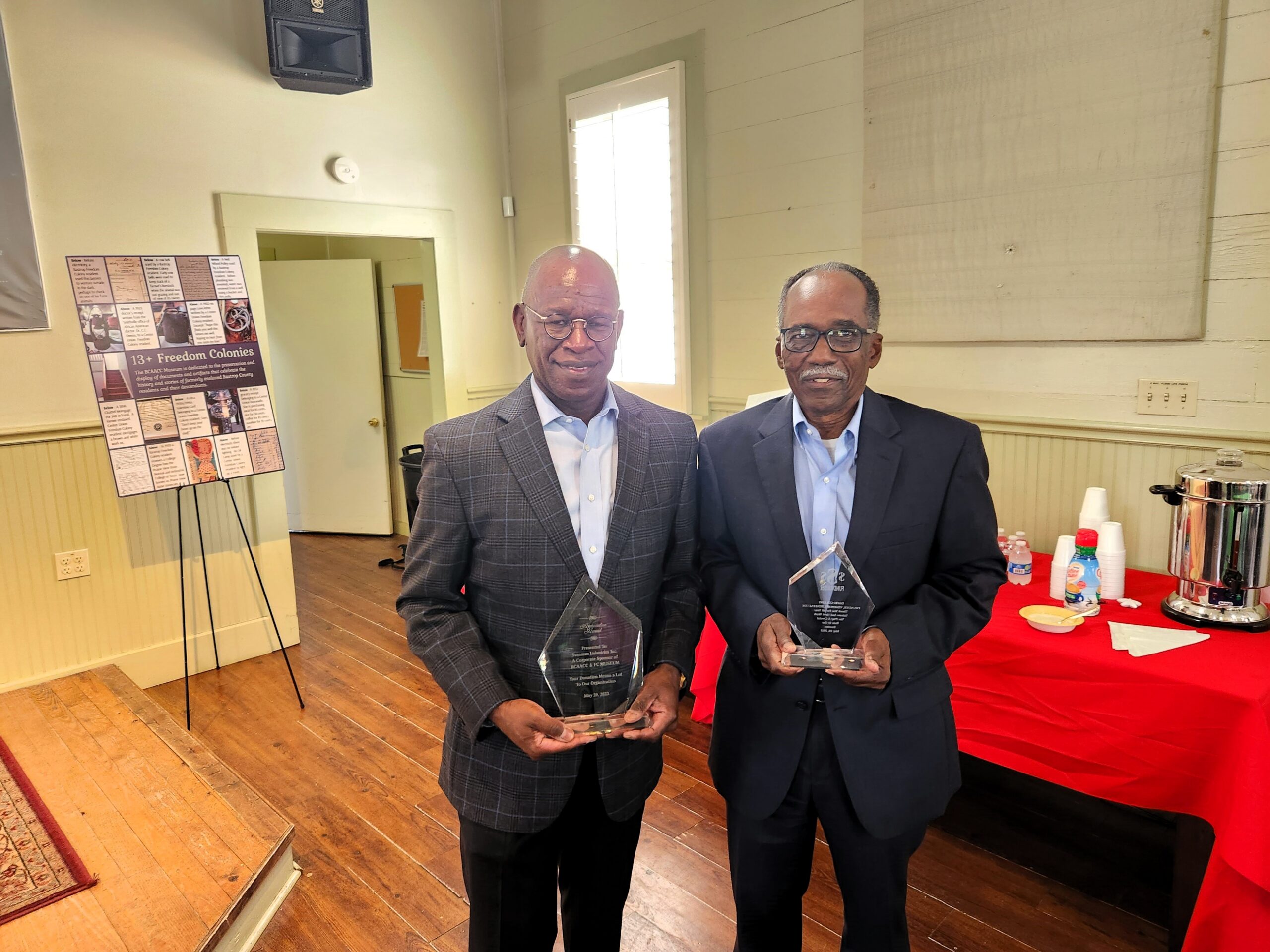 Two men holding glass awards in meeting room
