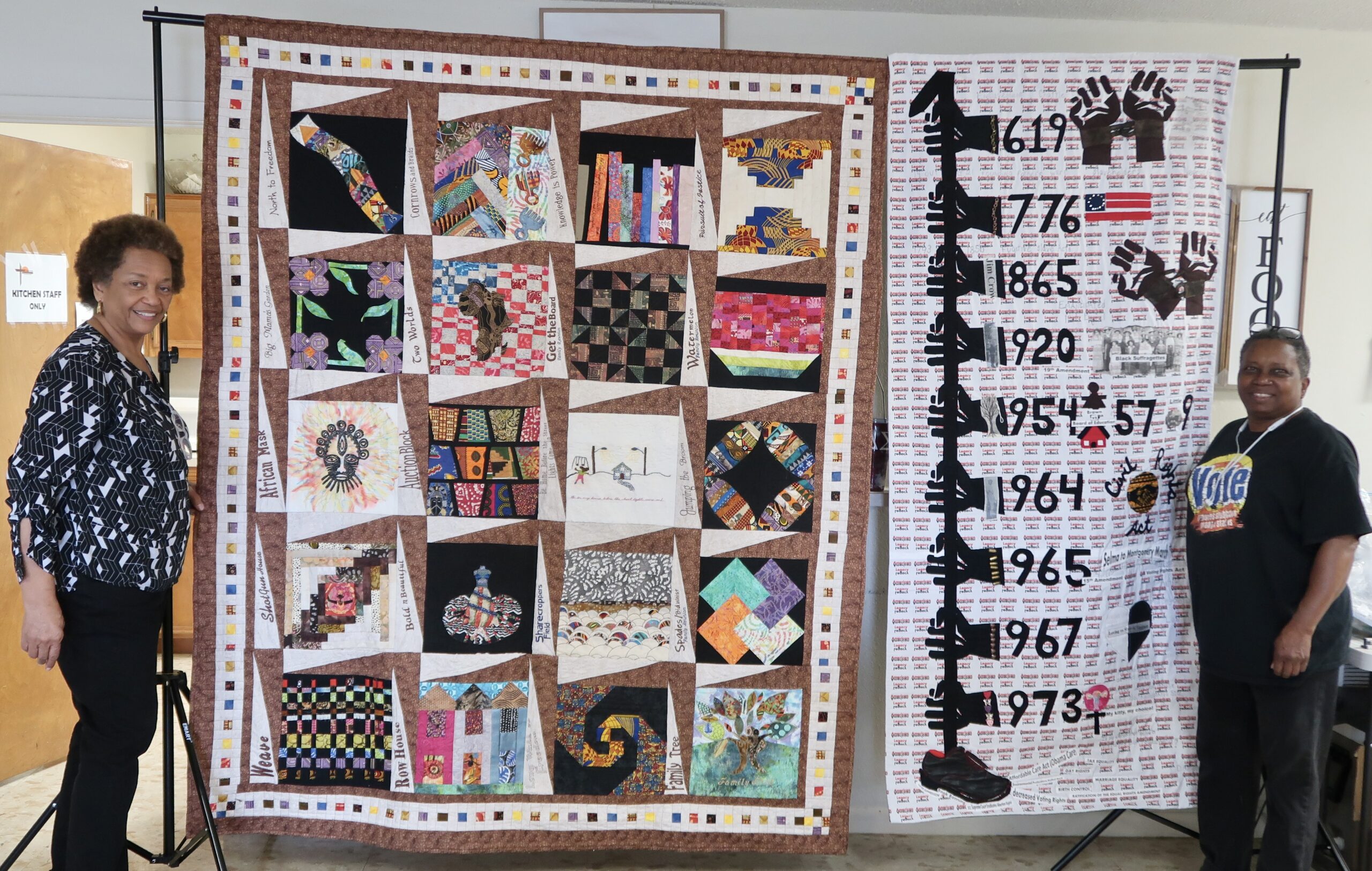 Two women display large commemorative patchwork quilt